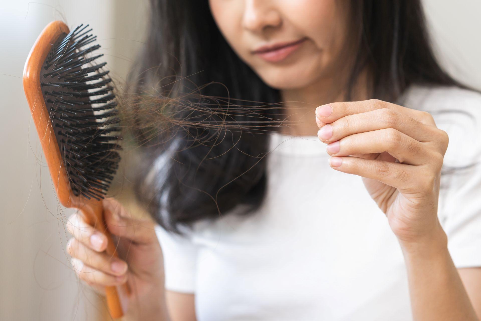 Frau haelt Haarbuerste mit ausgefallenen Haaren – typisches Anzeichen von Haarausfall